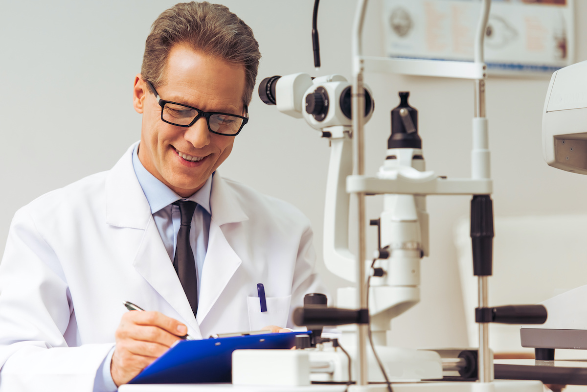 Handsome middle aged ophthalmologist making notes and smiling while sitting in his office; blog: Practice Solutions Beyond Medical Billing
