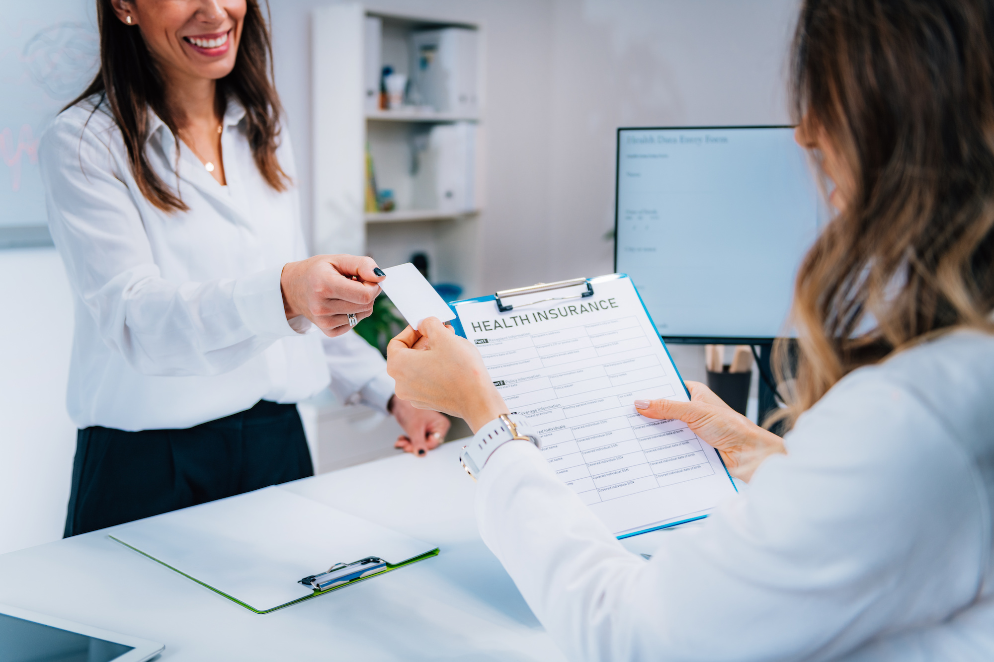Woman handing receptionist card for Medical Insurance at medical office front desk; blog: Traditional Medicare vs Medicare Advantage
